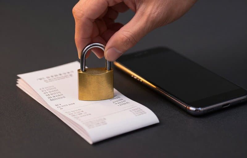 A hand closing a brass padlock over a stack of receipts beside a smartphone, illustrating revoking access after a Google Play purchase is voided