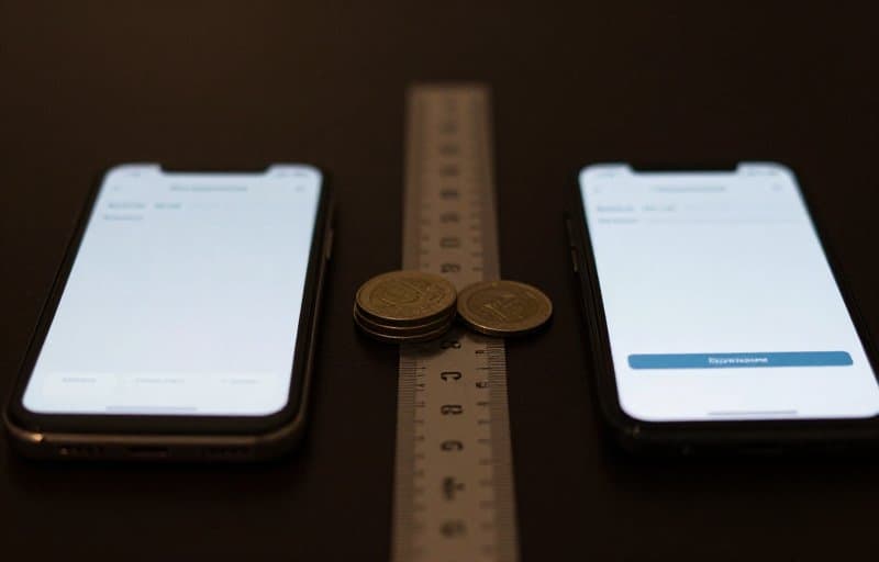 Two smartphones side by side on a dark desk showing subscription payment screens with a partial pile of returned coins between them, illustrating a full versus prorated subscription refund on the App Store and Google Play
